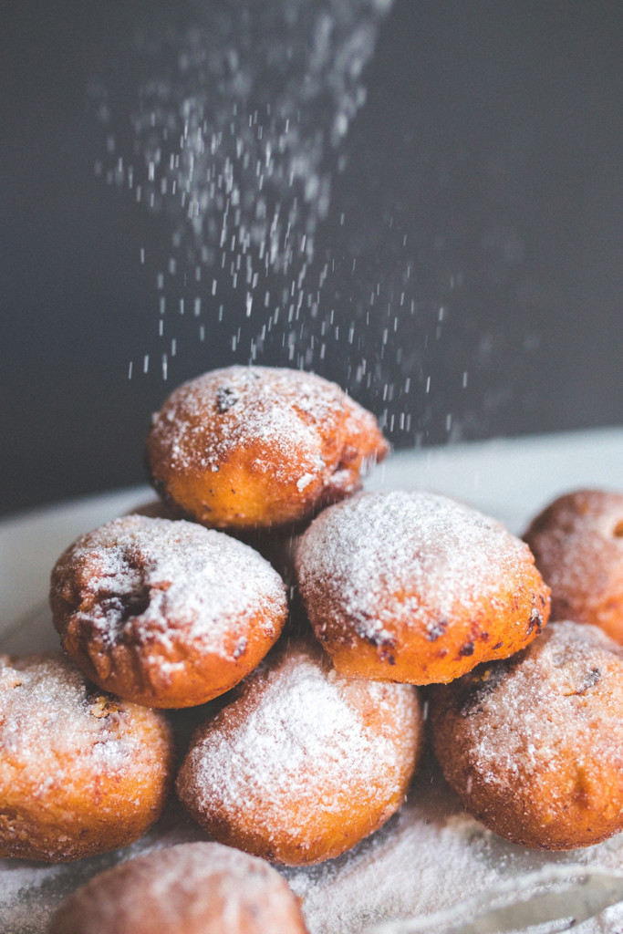 powdered sugar being sifted onto a pile of frittelle, an italian carnevale sweet treat